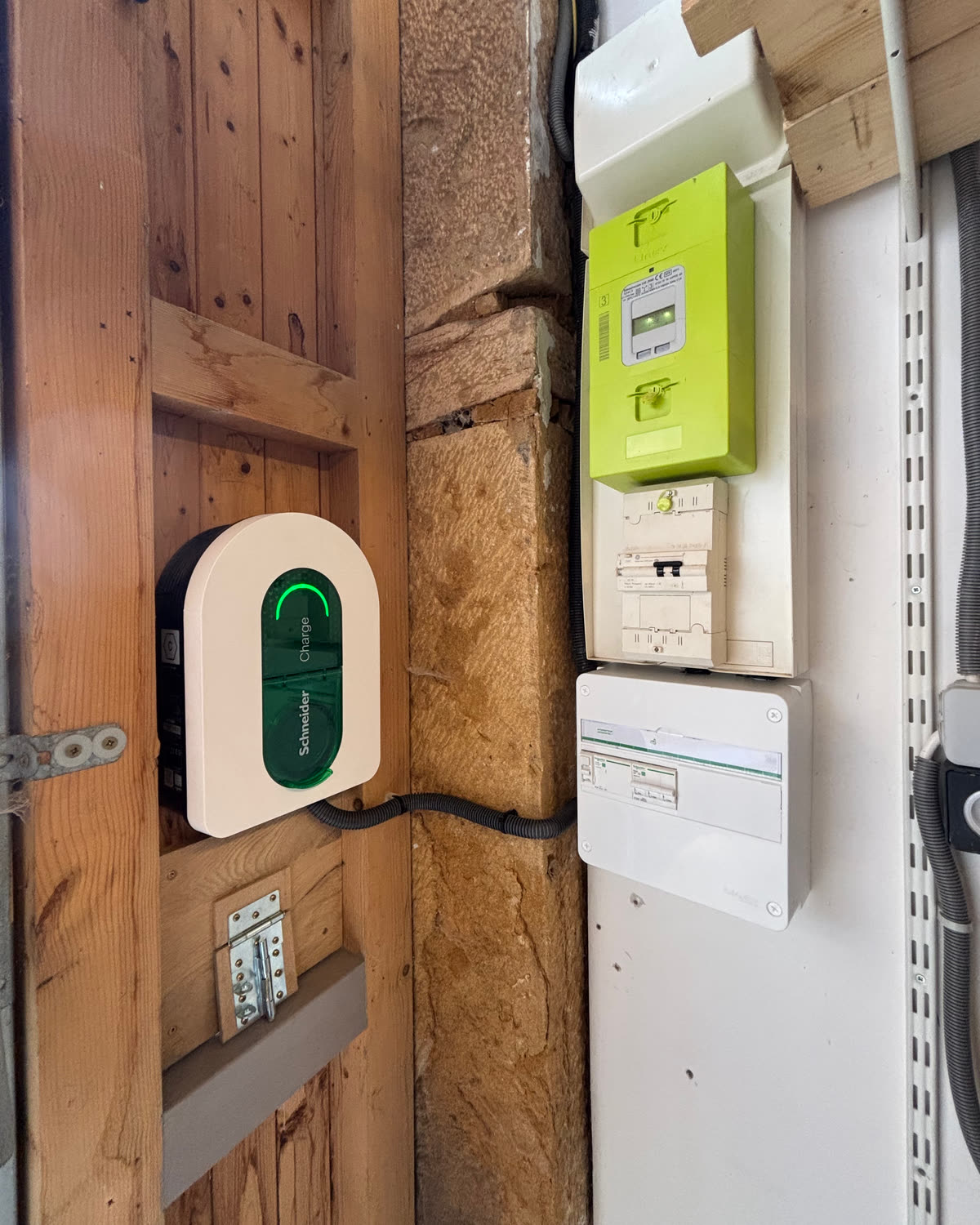 La borne murale sur l’ossature en bois du garage ; à droite, sur un mur blanc, le compteur Linky, le disjoncteur de branchement et un coffret électrique.